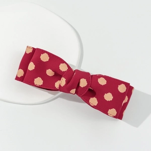 Detailed close-up of dark wine red polka dot bow hair clip with textured fabric finish