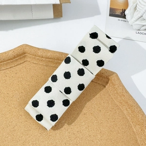 Polka dot bow hair clip with white and black fabric pattern on wooden tray background