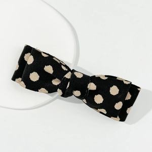 Close-up of elegant black hair clip with beige polka dots and textured fabric detail