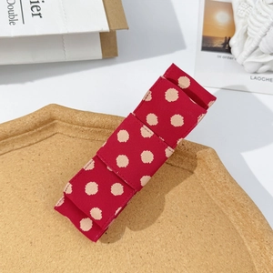 Close-up of a red polka dot ribbon bow hair clip on a textured display plate