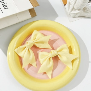 Detail of two yellow silk ribbon bow hair clips on a ceramic plate for girls