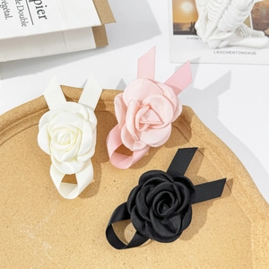 Détail des barrettes camélia en satin blanc, rose et noir posées sur un plateau bois