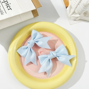 Close-up of two light blue satin bow hair clips featuring fine texture and layered design