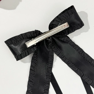 Dettaglio del fiocco in raso nero con pizzo arricciato e clip a becco d'anatra in metallo