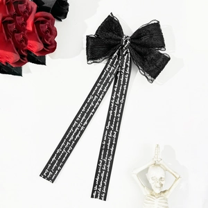 Detailed macro view of dark Gothic lace bow hairpin with long lettered ribbons and skull decor