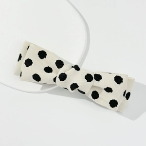 Elegant off-white bow hair clip with black polka dots on ribbed fabric from a 45-degree angle