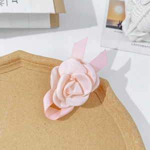 Détail d'une pince à cheveux camélia en satin rose avec rubans sur un plateau texturé