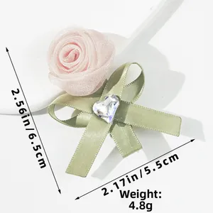 Detalle de una pinza para el pelo de rosa rosa en organza con lazo verde y cristal corazón