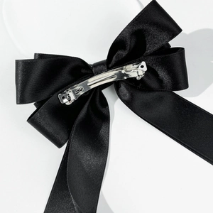 Close-up of black satin double bow hair clip with long ribbons and metal spring clasp