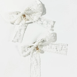 Close-up of white lace bow hair clips with elegant pearl pendants and golden metal accents
