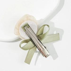 Detalle de lazo de satén verde claro y flor de organza con clip de metal plateado