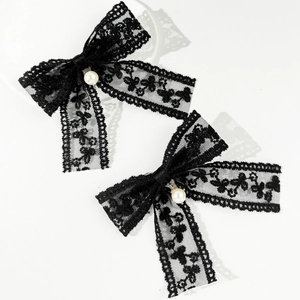 Detailed view of two black lace bow hair clips with white pearls on a white background