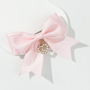 Detail von rosa Satin-Schleifen-Haarspange mit Perlenherz-Anhänger auf weißem Sockel