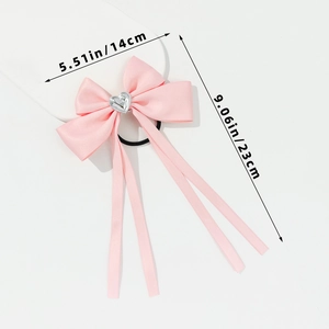 Detail view of pink satin bow hair tie with silver heart and long ribbon streamers