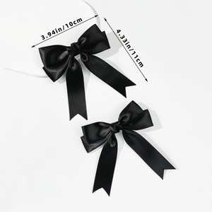 Detail showing two black satin bow hair clips with soft silk texture and 10x11cm dimensions
