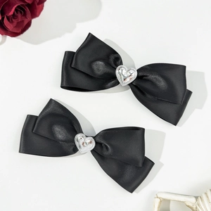 Détail de barrettes nœud en satin noir avec cristal en forme de cœur sur fond ivoire
