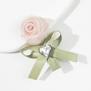 Pinza para el pelo con rosa de organza rosa, lazo verde y cristal corazón en fondo blanco