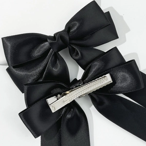Detail of two black satin ribbon bow hair clips with long streamers and metal duckbill clips