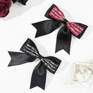 Close-up of black and burgundy ribbon bow hair clips with gothic script on satin fabric