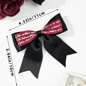 Detail shot of a black satin bow hair clip with red ribbon and white cursive text