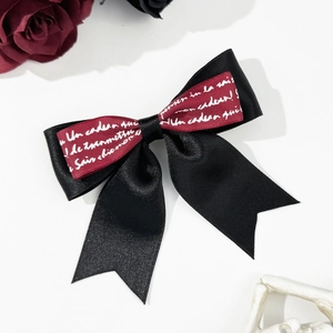 Detail of a black and dark red bow hair clip with white French script on satin ribbons
