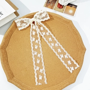 Detail of white lace bow hair clip with floral embroidery on elegant long ribbons