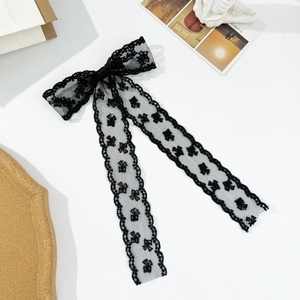 Detailed texture of black lace bow hair clip with embroidered ribbon and wavy edges
