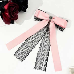 Dettaglio macro del fiocco in raso rosa con pizzo nero, strass a cuore e lunghi nastri