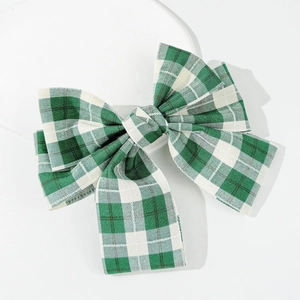 Close-up of green plaid bow hair clip with detailed woven fabric texture on white background
