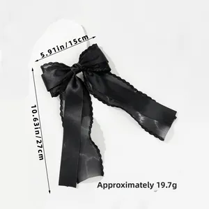 Elegant black satin hair bow with lace edges and long ribbons on stone display stand