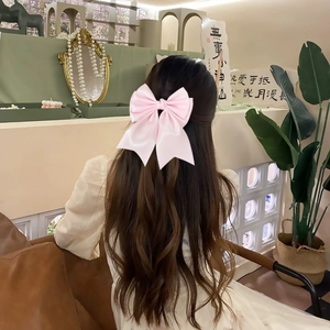Detail of a large pink satin bow hair clip styled on elegant wavy brown hair