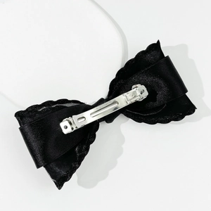 Close-up of black satin bow hair clip showing silver metal spring fastener and wavy texture