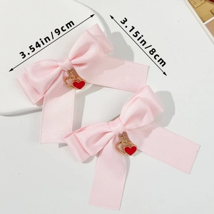 Détail de barrettes à nœuds en satin rose avec pendentifs cœur rouge et doré et tailles