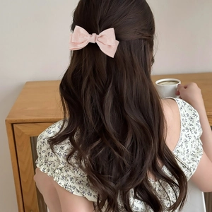 Elegant light pink fabric bow hair clip worn by a model with long brown wavy hair