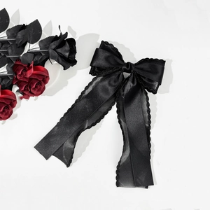 Detail of black satin bow hair clip with long ribbons and elegant wavy lace edges