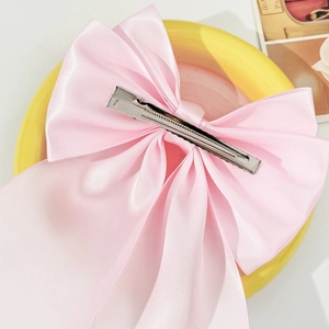 Detail of a large pink satin bow hair clip with a sturdy silver metal duckbill clip back