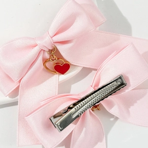 Détail du nœud en satin rose avec pendentif cœur rouge et pince à bec de canard en métal