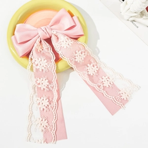 Detailed view of pink satin hair clip with white floral lace embroidery and long ribbons