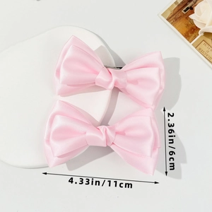 Vue détaillée de deux barrettes à nœuds en satin rose avec dimensions de 11 cm par 6 cm