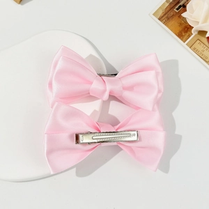 Vue détaillée de deux barrettes à nœuds en satin rose clair avec pinces crocodiles en métal