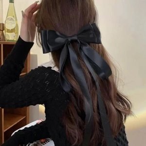 Rear view of a model wearing a large black satin bow hair clip with long flowing ribbons