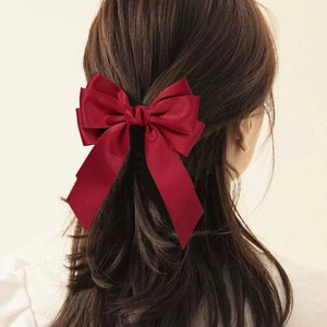 Detail showing red satin double-layered bow hair clip with streamers on long wavy hair