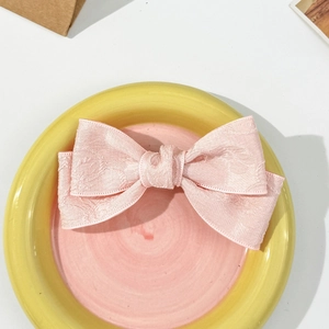 Detailed macro view of pink floral jacquard ribbon bow hair clip on ceramic plate