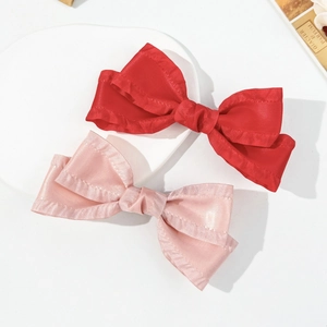 Detail of red and pink satin bow hair clips with ruffled edges on a white display board