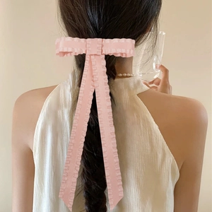 Detail of a light pink ruffled bow hair clip with long ribbons on braided hair