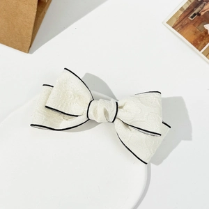 Detail view of cream bow hair clip with black edges and intricate floral jacquard fabric