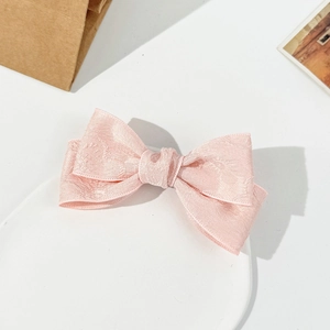 Close-up of pink bow hair clip with elegant jacquard texture and layered fabric design