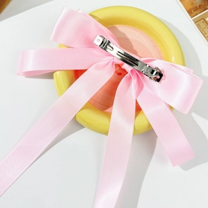 Detail of light pink satin bow hair clip with silver spring metal fastener on ceramic tray