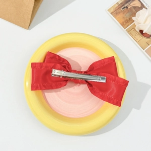 Close-up of a red silk bow hair clip with ruffled edges and a silver metal duckbill clip
