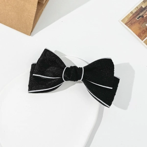 Elegant black velvet bow hair clip with white piping displayed on a white tray